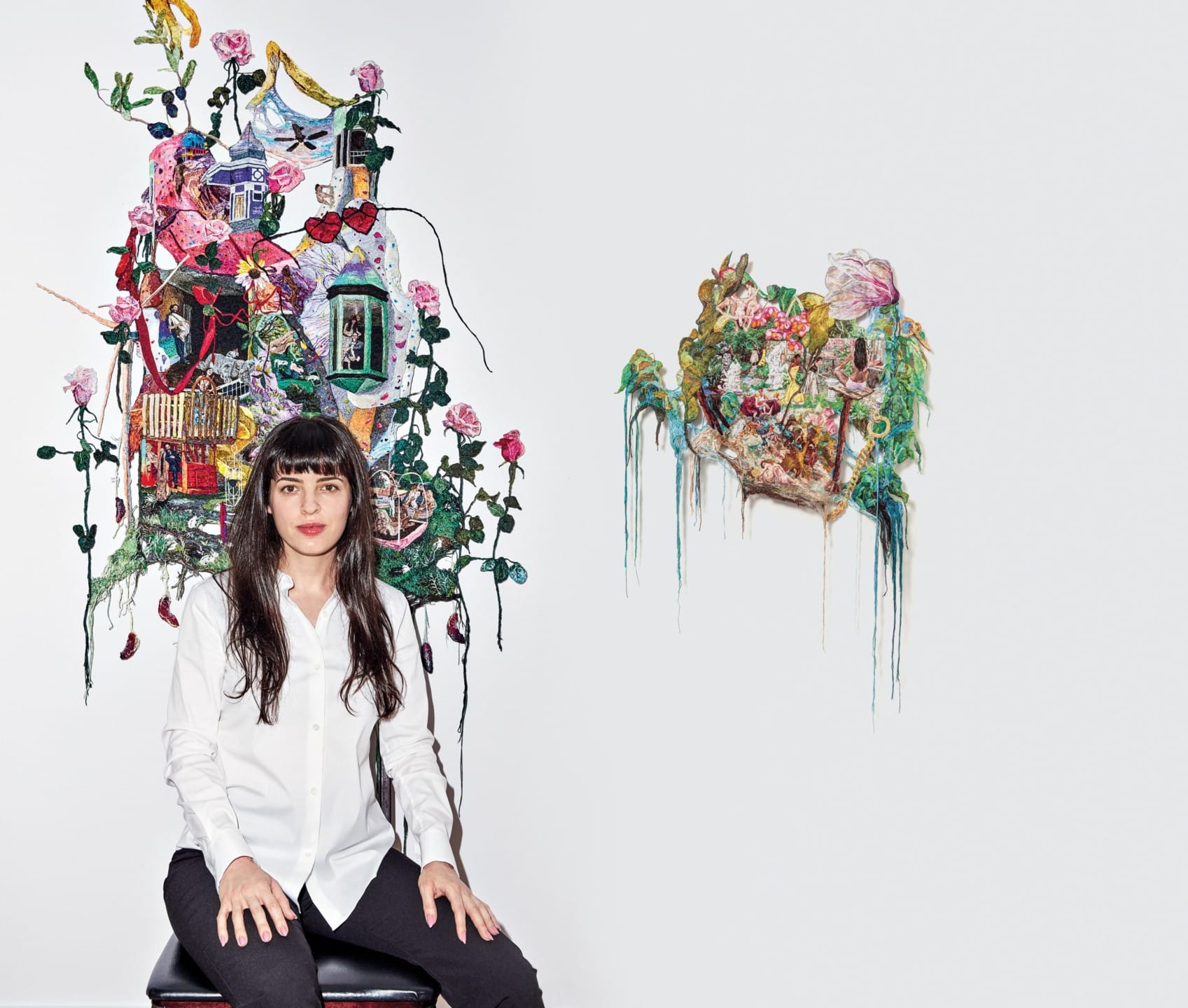 Person seated in front of colorful textile artwork displayed on a white wall.