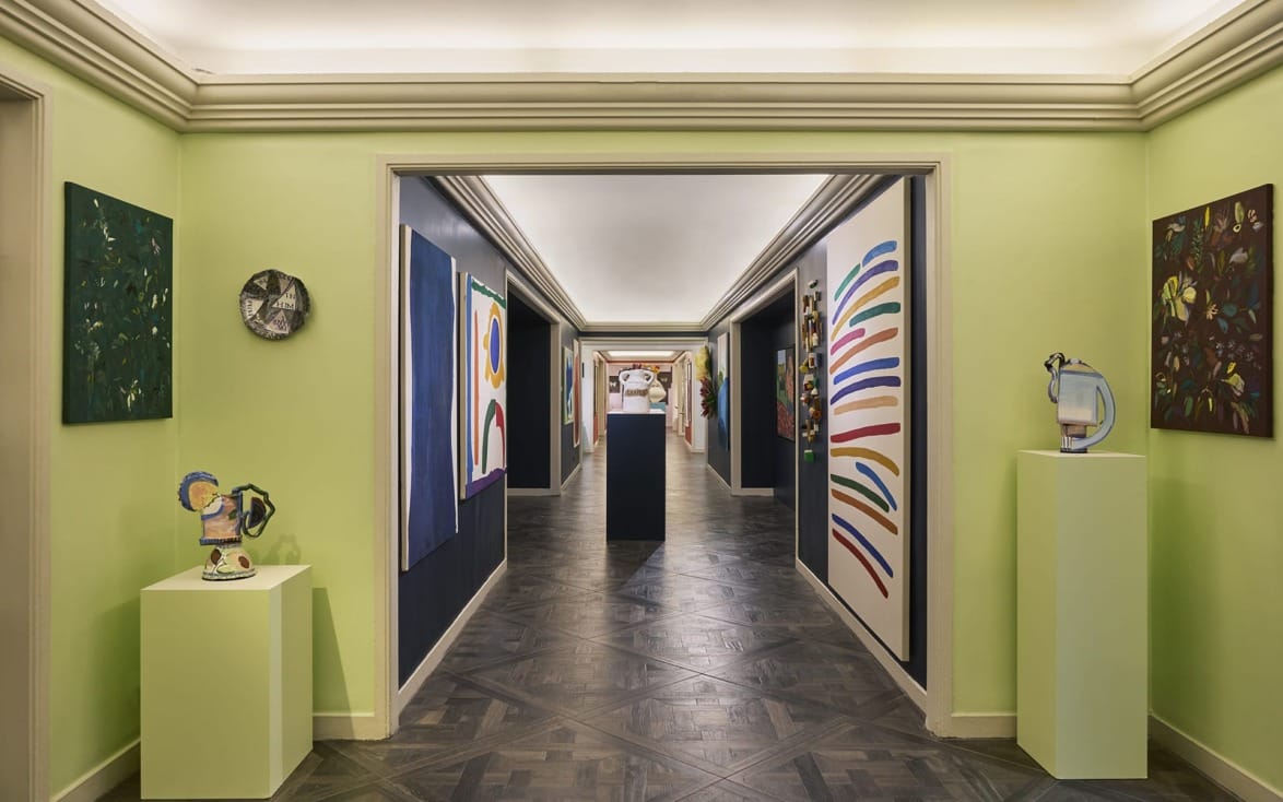 Art gallery hallway with colorful abstract paintings on lime green walls and sculptures on pedestals.
