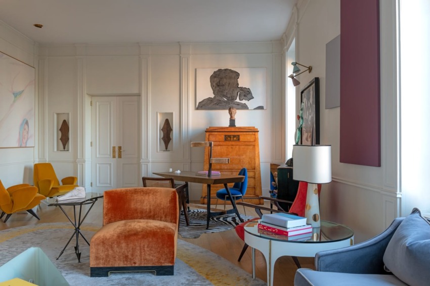 Modern living room with colorful chairs, abstract wall art, wooden furniture, and a variety of decor elements.