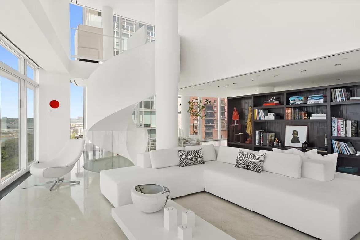 Modern living room with white decor, spiral staircase, large windows, and shelves filled with books and decorative items.
