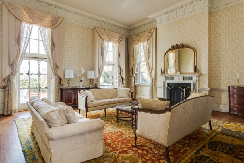 Elegant living room with classic furniture, large windows, ornate fireplace, and patterned rug.