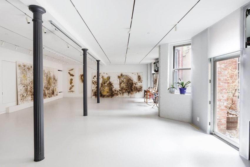 Minimalist art gallery interior with wall artwork, large windows, and gray pillars. Bright and airy space with white walls.