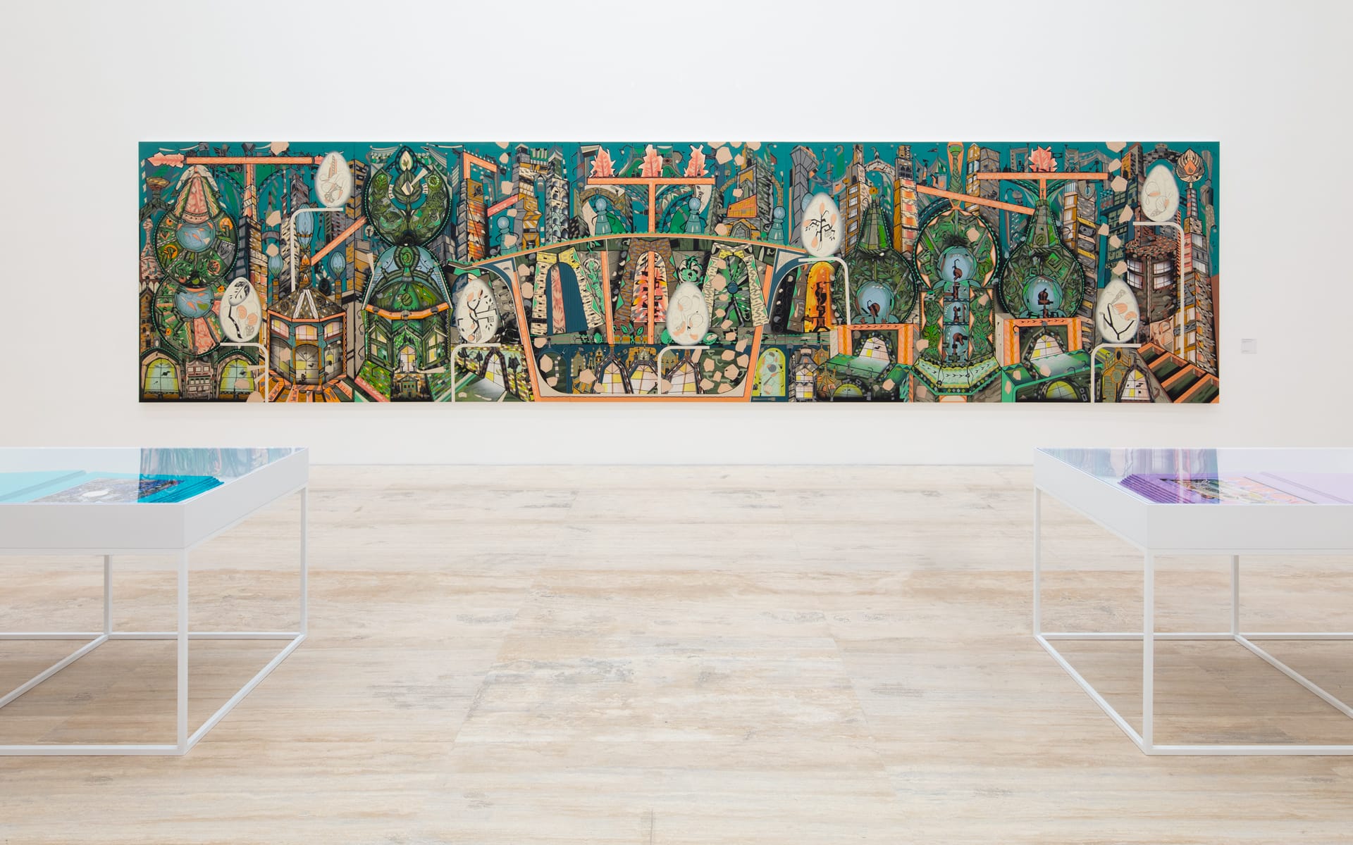 Large, colorful mural with intricate designs on a gallery wall, surrounded by light wood flooring and minimalistic display tables.