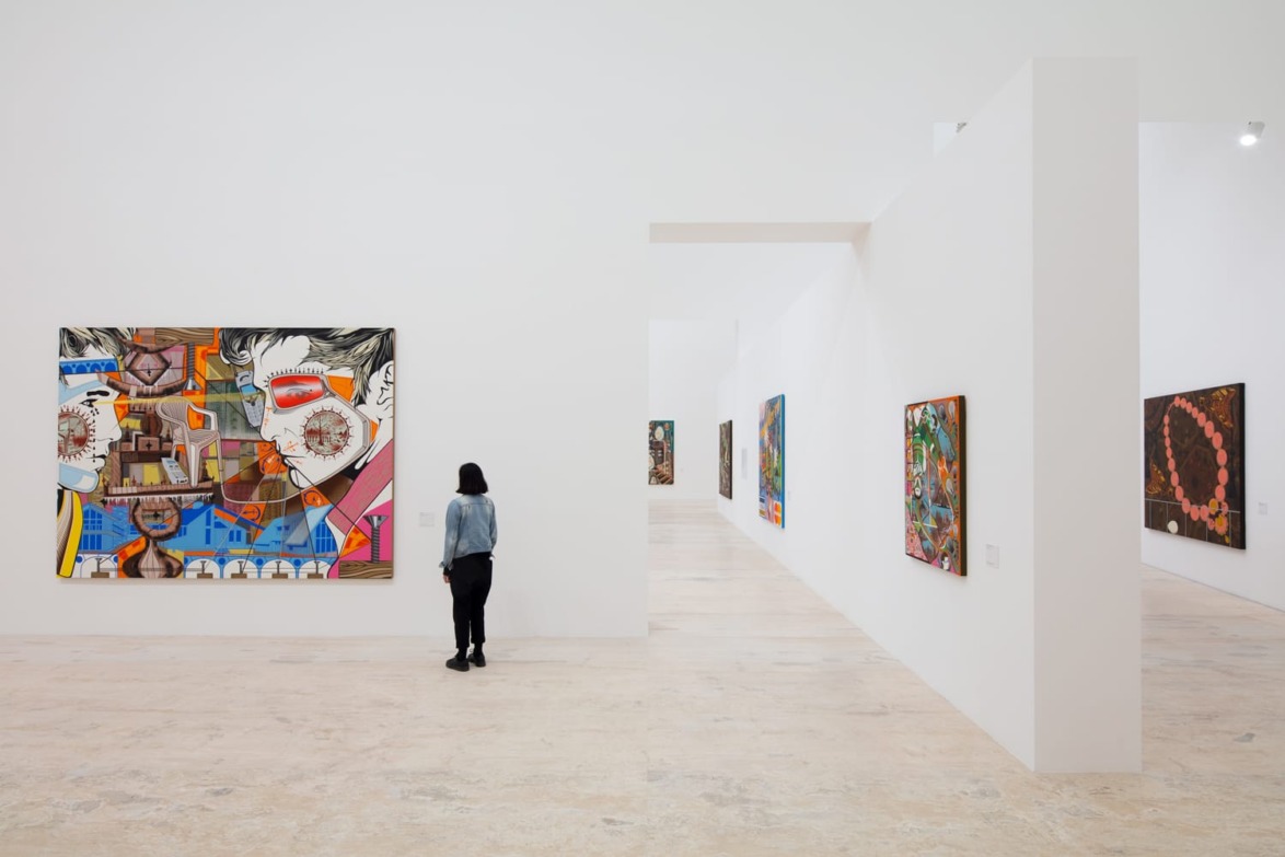 Person viewing colorful paintings in a modern art gallery with white walls and minimalistic design