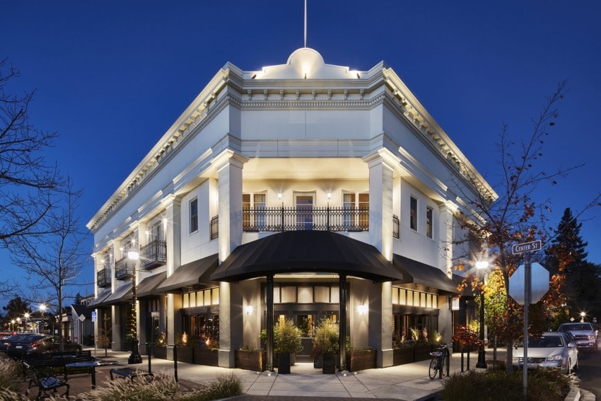 Beautifully illuminated corner building with elegant architecture, trees, and street lamps at dusk.