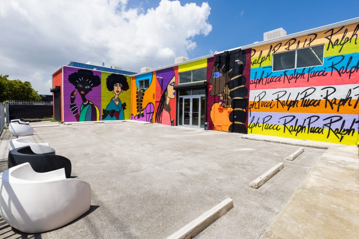Vibrant mural on building exterior featuring diverse portraits and colorful patterns under a clear sky.