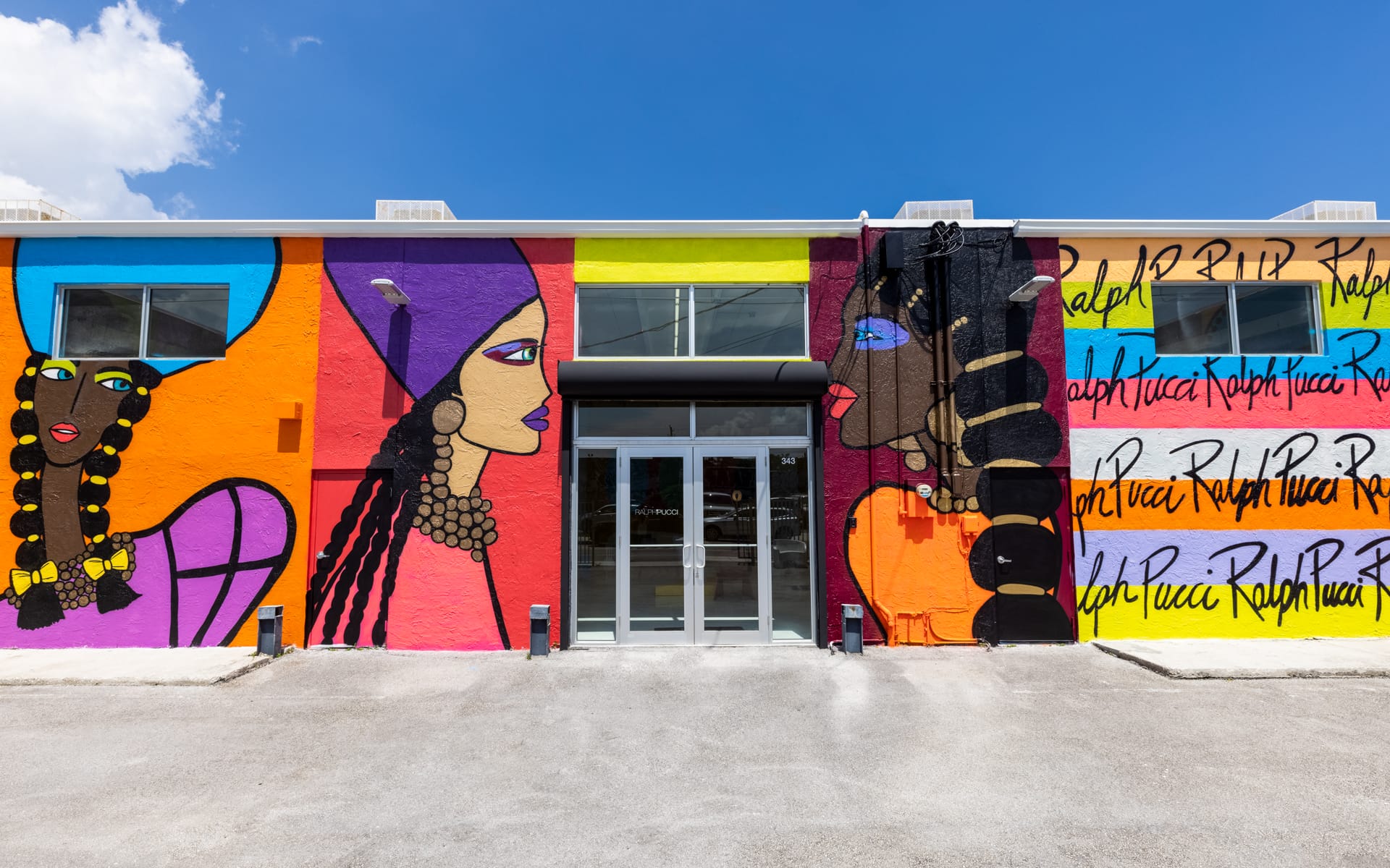 Colorful mural on a building exterior featuring stylized portraits of women with vibrant backgrounds and intricate patterns.