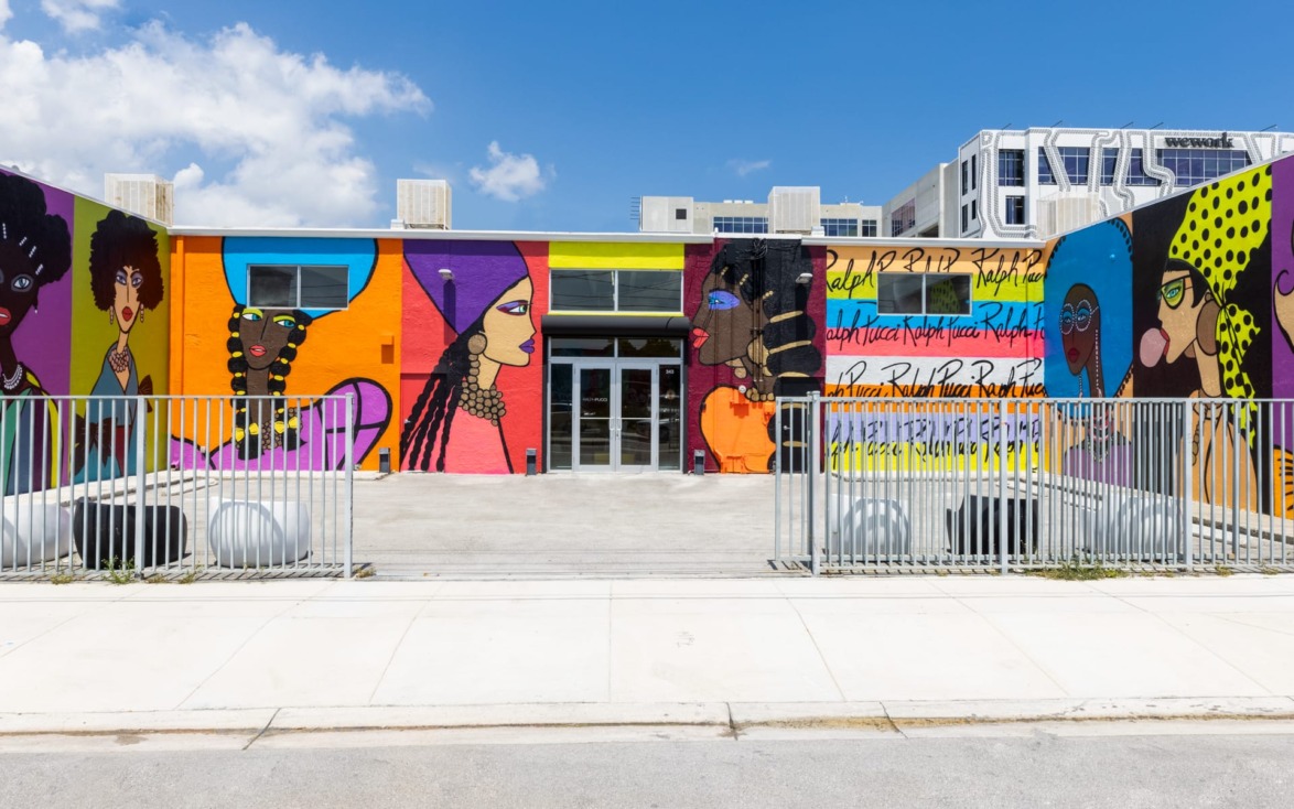 Colorful mural featuring diverse women on a building exterior in a sunny urban setting with a clear blue sky.