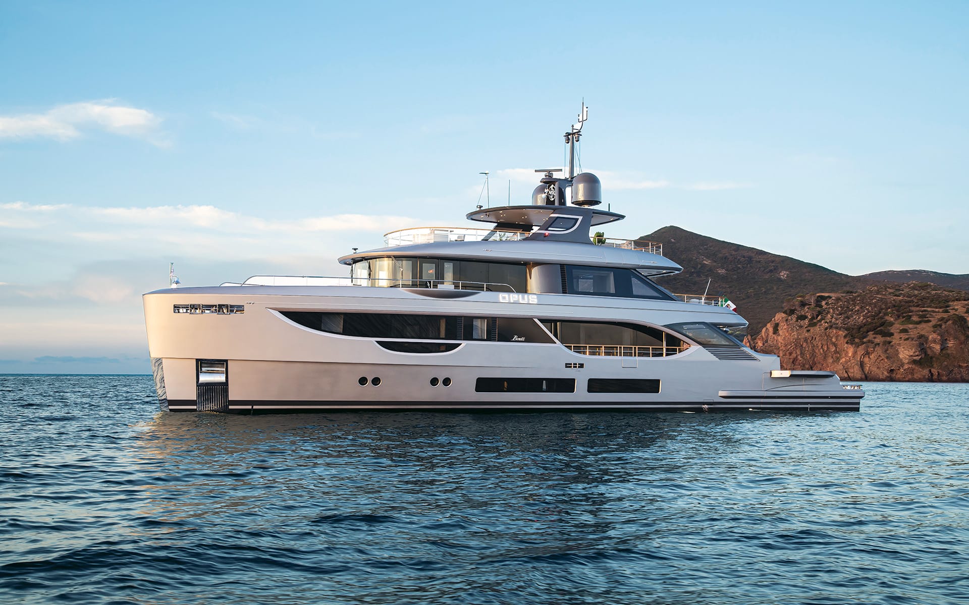 Luxurious yacht sailing near rocky coastline under a clear blue sky.
