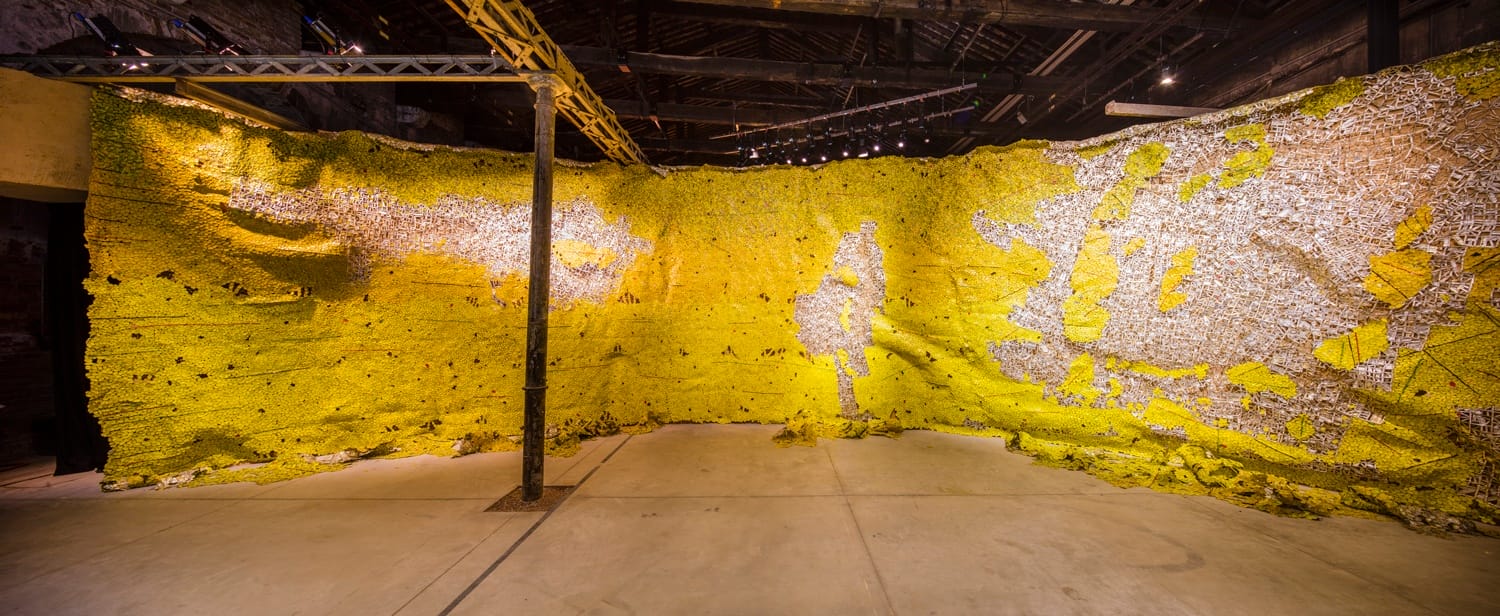 Yellow and silver abstract art installation on a curved wall in an industrial-style gallery space.