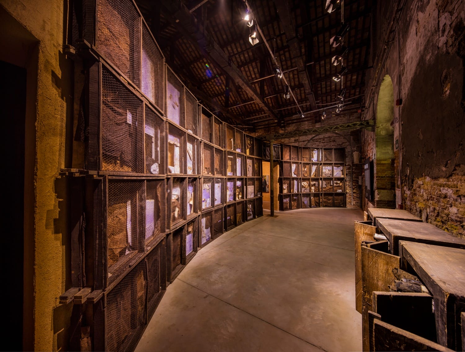 Dimly lit, arched interior corridor with rustic wooden shelves lining the walls and a concrete floor.