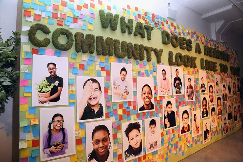Wall display with colorful sticky notes and photos of smiling children under the question "What does a healthy community look like to you?"
