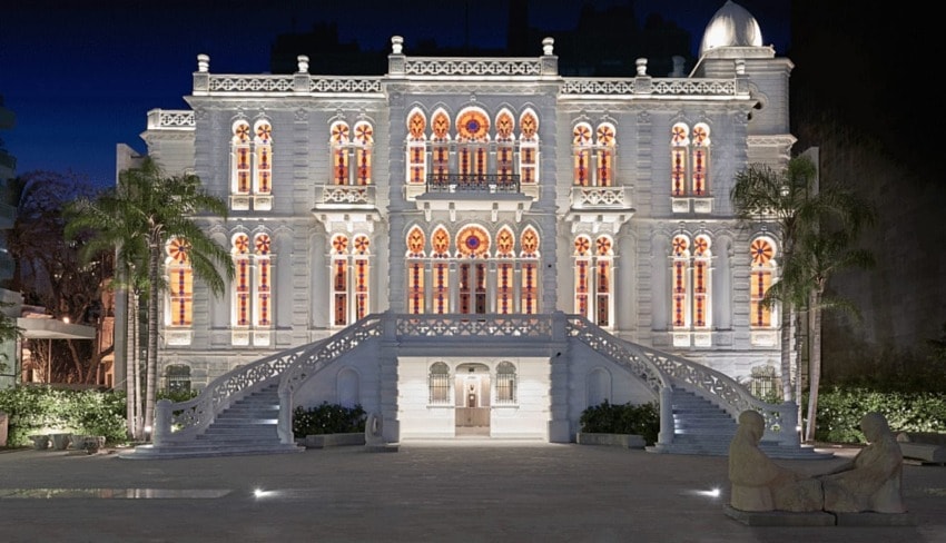 Illuminated historic building at night with ornate architecture, large staircase, and trees in the foreground.