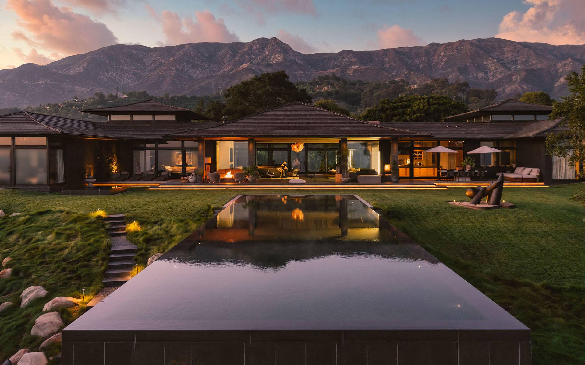 Luxury home with a reflecting pool, warm lighting, and mountain backdrop at sunset.