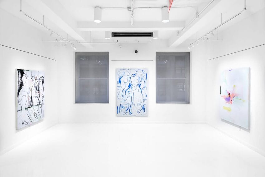 Minimalistic art gallery with three abstract paintings displayed on white walls under bright lighting.