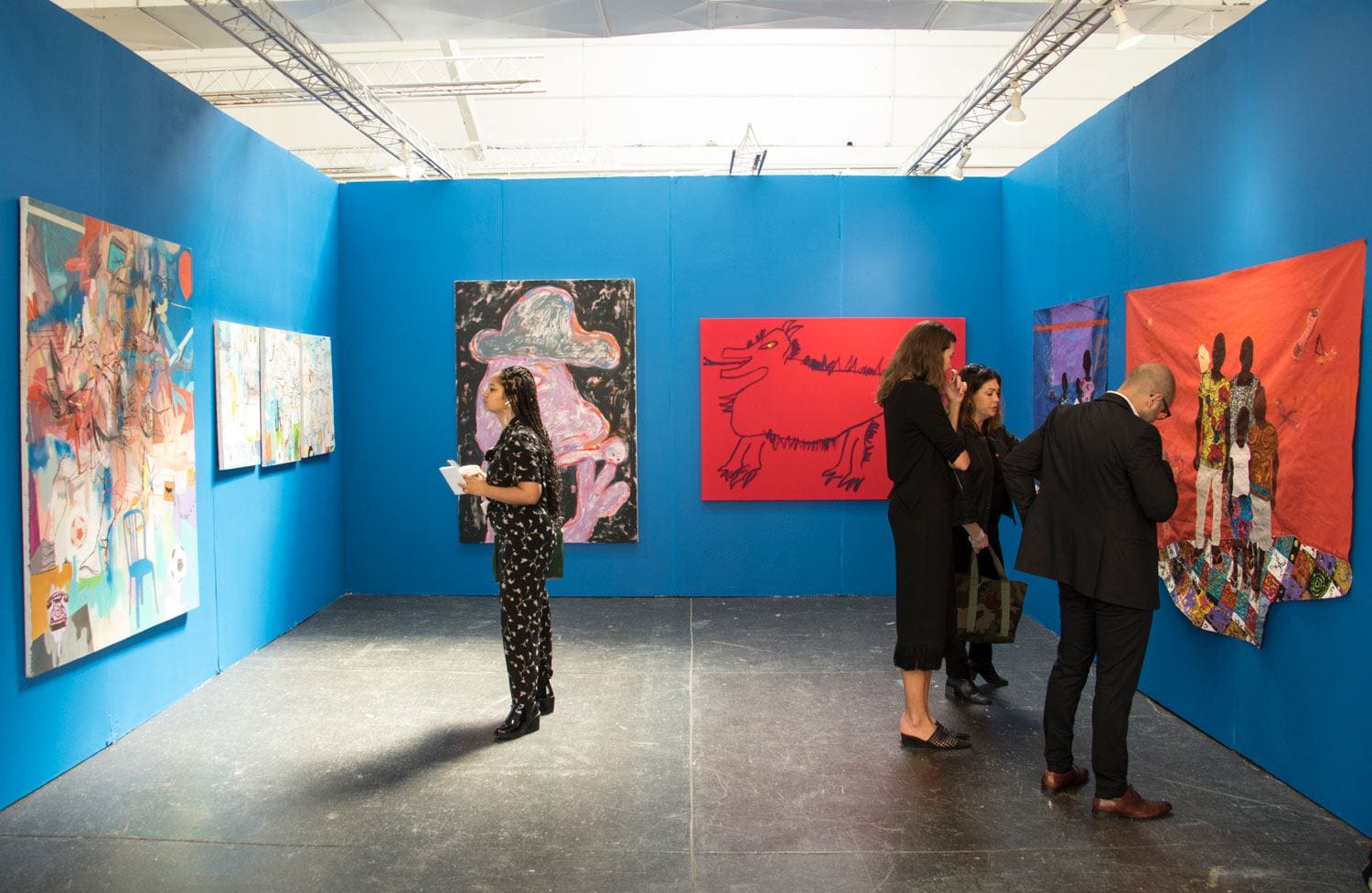 People viewing colorful abstract art in a bright blue-walled gallery exhibition.