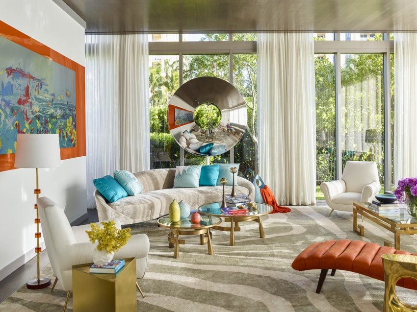 Contemporary living room with modern furniture, vibrant artwork, round mirror, and large windows with sheer curtains.