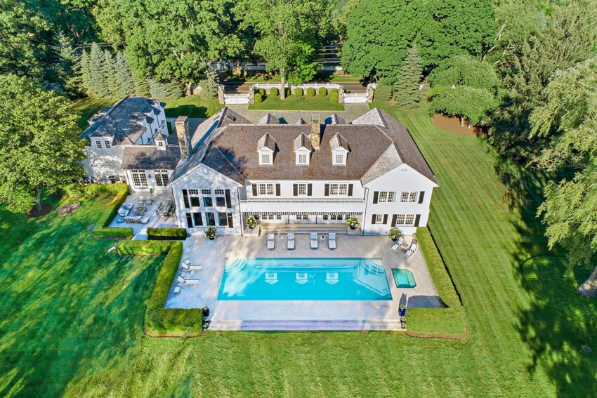 Aerial view of a large estate with a pool, surrounded by lush greenery and well-manicured lawns.