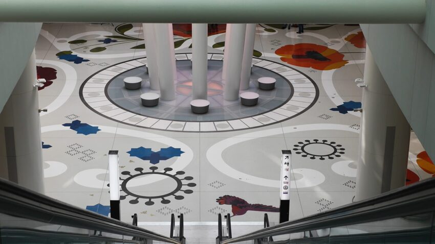 Colorful geometric floor design with floral patterns and cylindrical pillars viewed from an escalator.