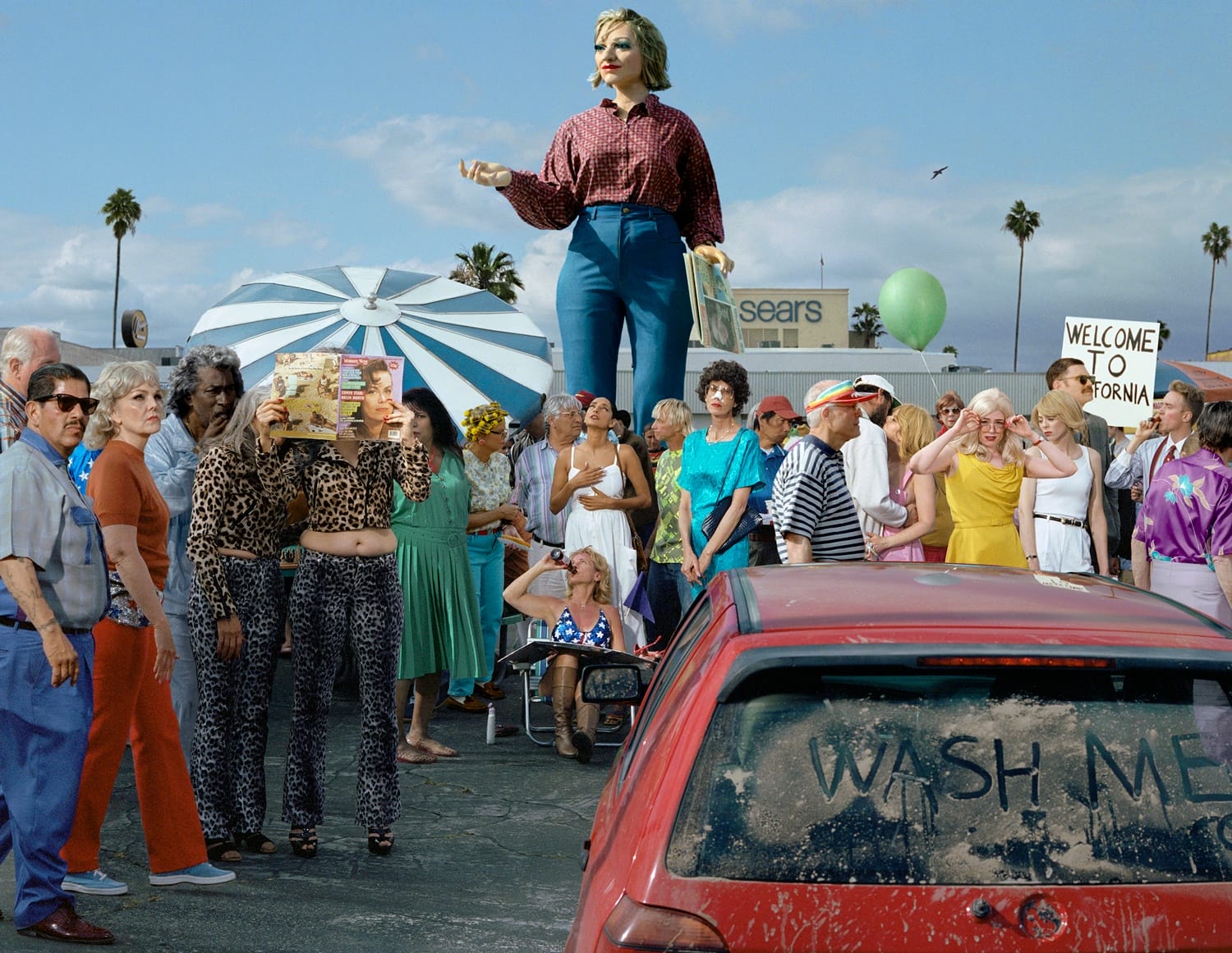 A surreal scene with a giant mannequin and people in a crowded outdoor area, featuring a car with "Wash Me" on the window.