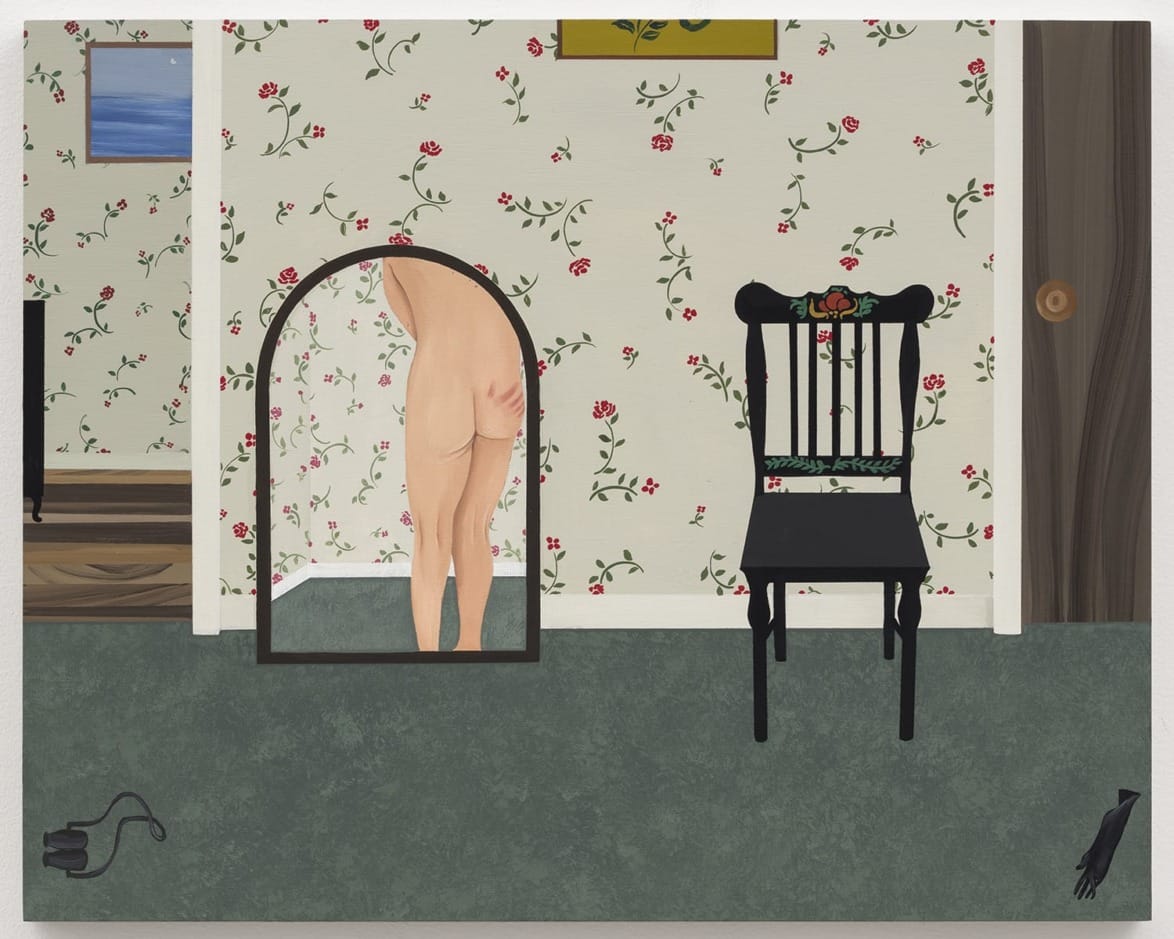 A person standing in front of a mirror with a floral wallpaper background, a black chair, and a small painting on the wall.