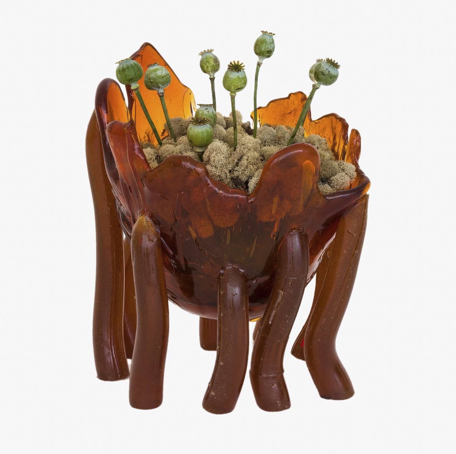 Creative brown glass sculpture with green plant-like elements, resembling a spider-like structure, on a white background.