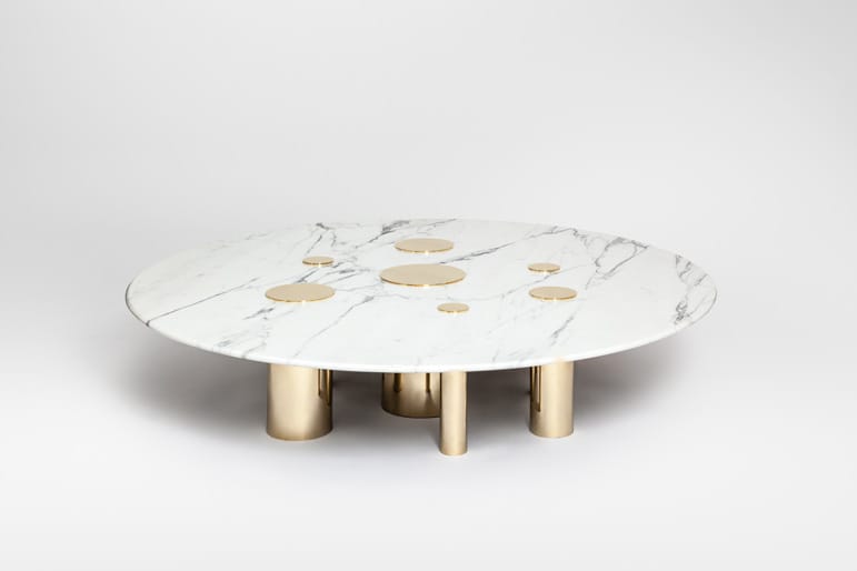 Round marble coffee table with gold cylindrical legs and circular gold accents on the surface.
