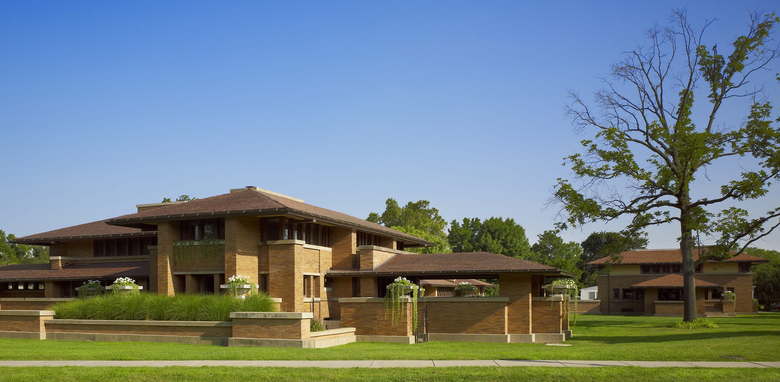 Frank Lloyd Wright's iconic prairie-style Robie House with a green lawn and clear blue sky.