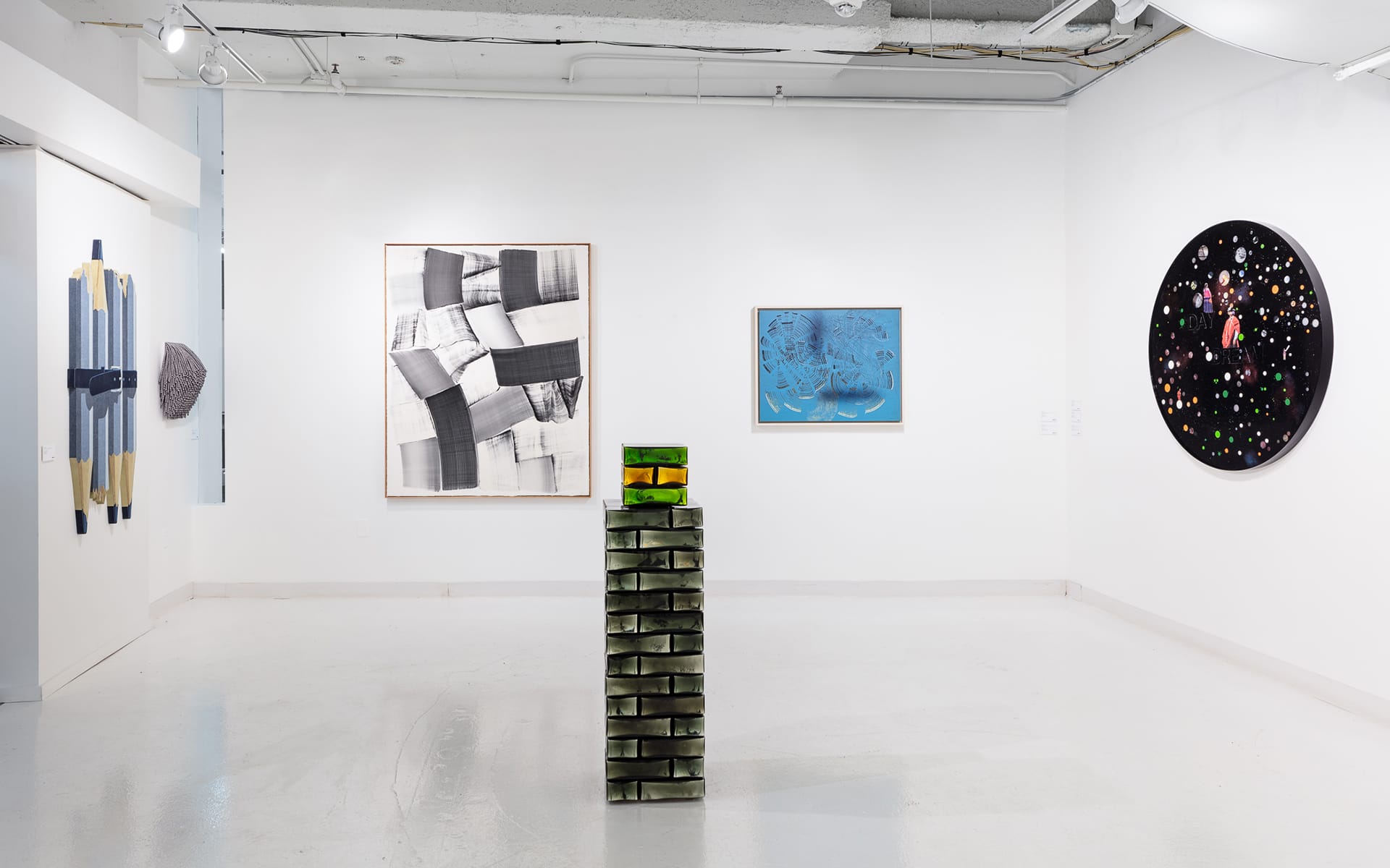 Contemporary art gallery with abstract paintings on walls and a green stacked sculpture in the center of the white room.