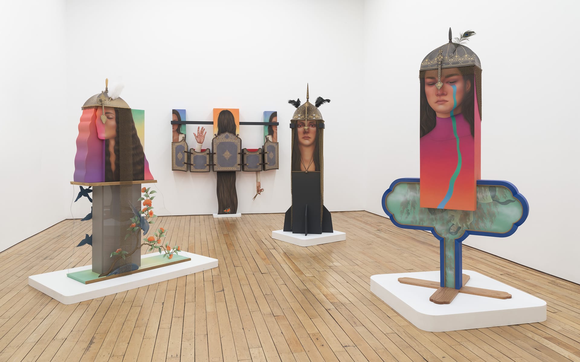Colorful sculptures of abstract human figures with helmets in a modern art gallery on a wooden floor.