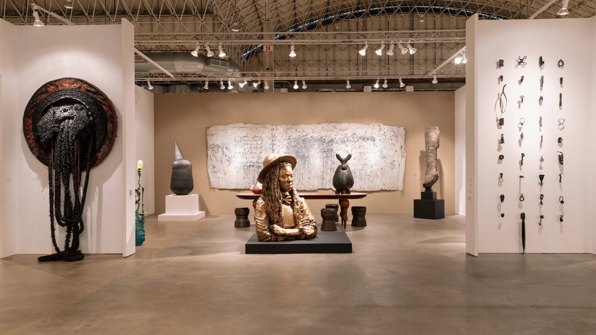 Art gallery interior displaying various sculptures and wall-mounted art pieces under a high, arched ceiling.