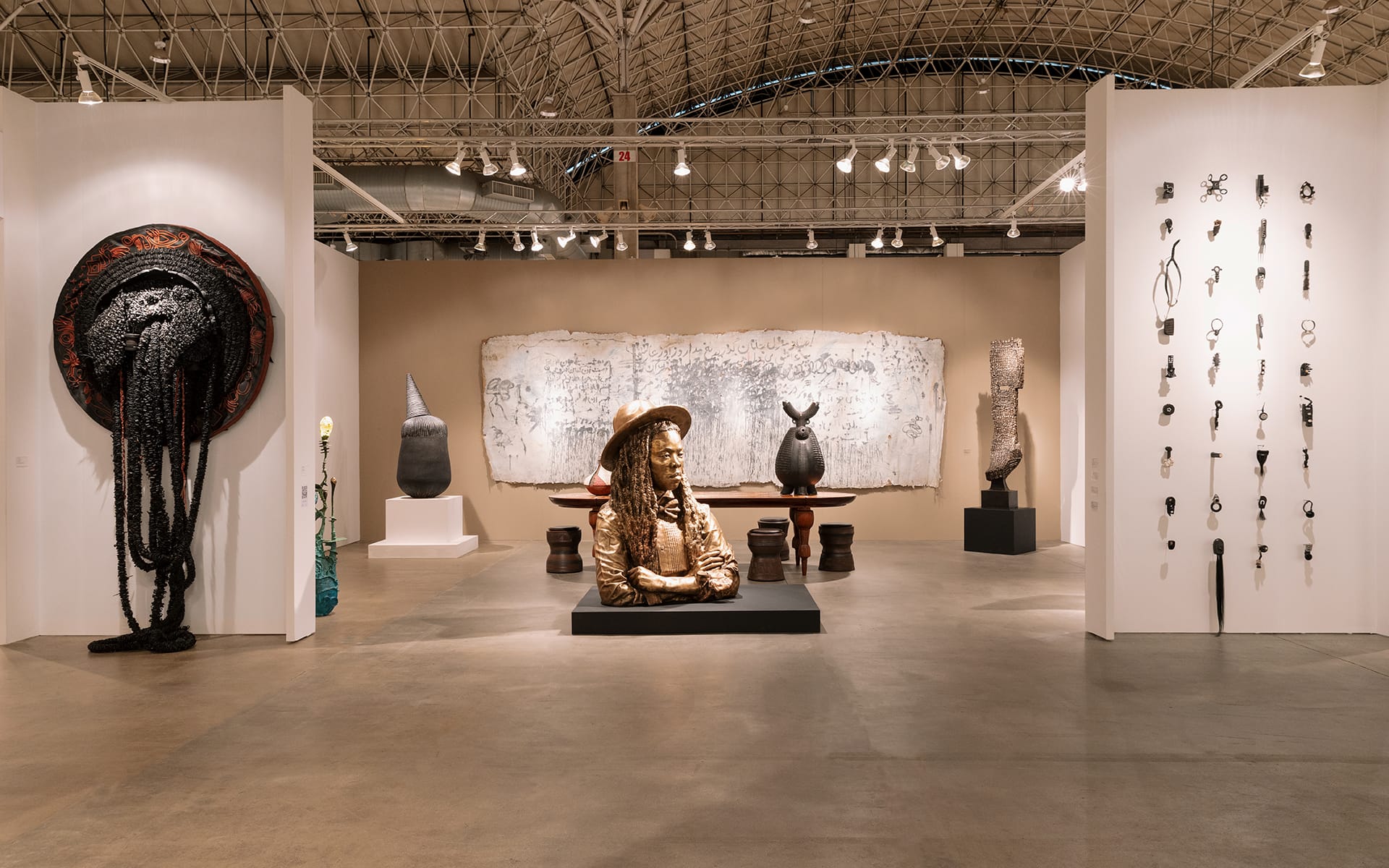 Art gallery interior displaying various sculptures and wall-mounted art pieces under a high, arched ceiling.