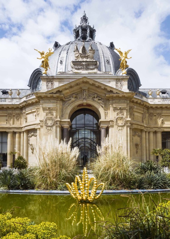 Exterior view of Petit Palais in Paris with golden sculptures and green vegetation in the foreground.
