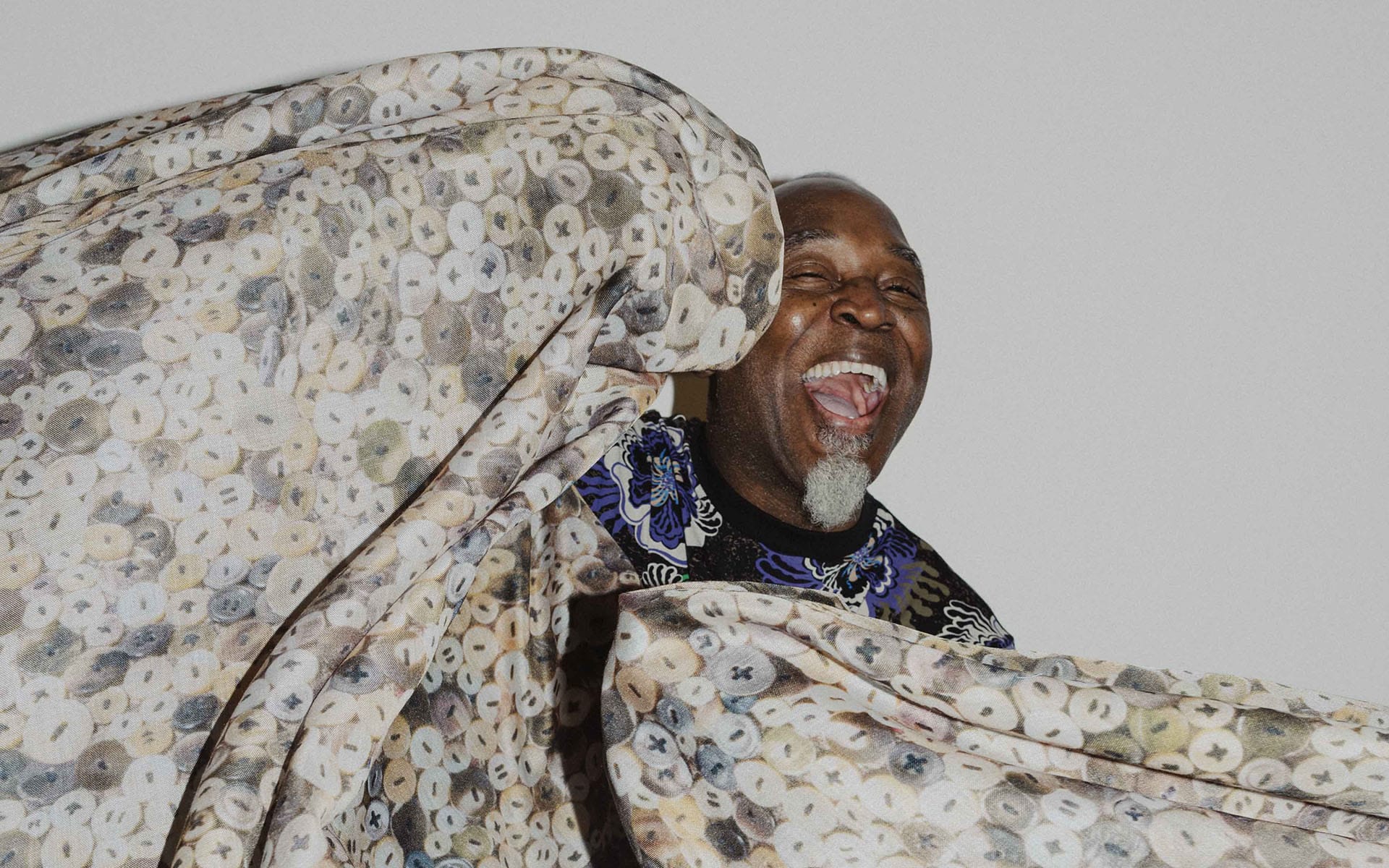 Man joyfully laughing behind a patterned fabric swirling in motion.