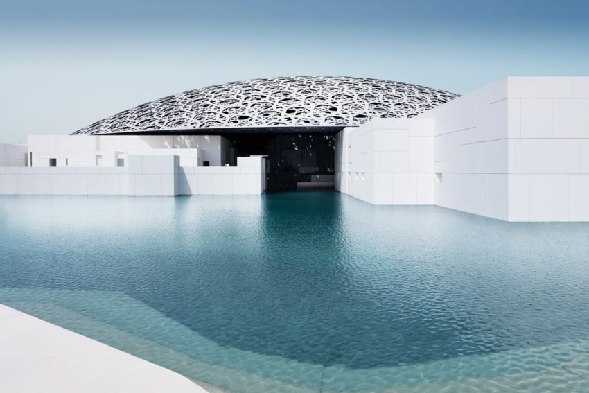 Modern architectural building with a patterned dome roof, surrounded by water under a clear blue sky.