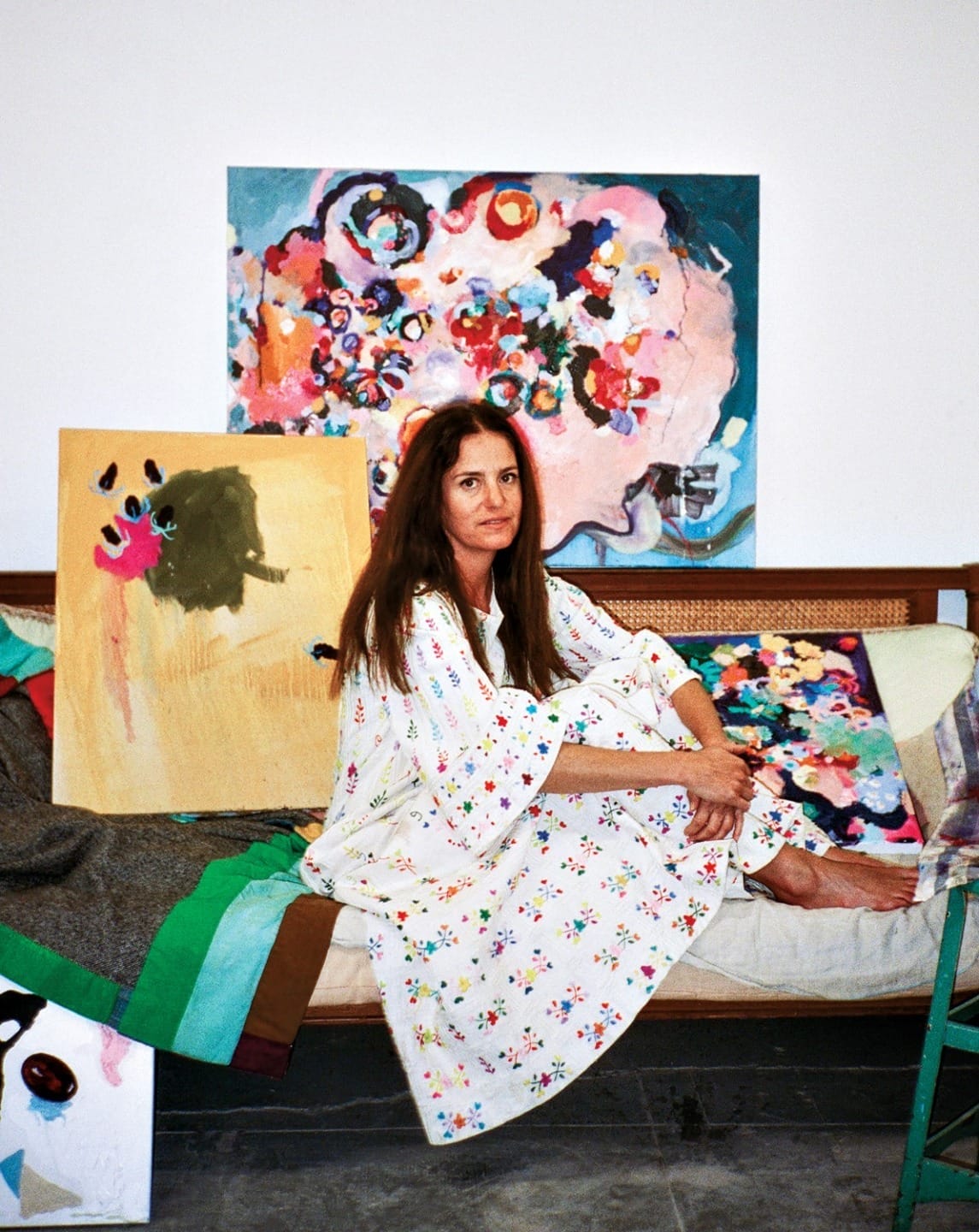 Artist sitting on a couch surrounded by colorful abstract paintings in a studio.