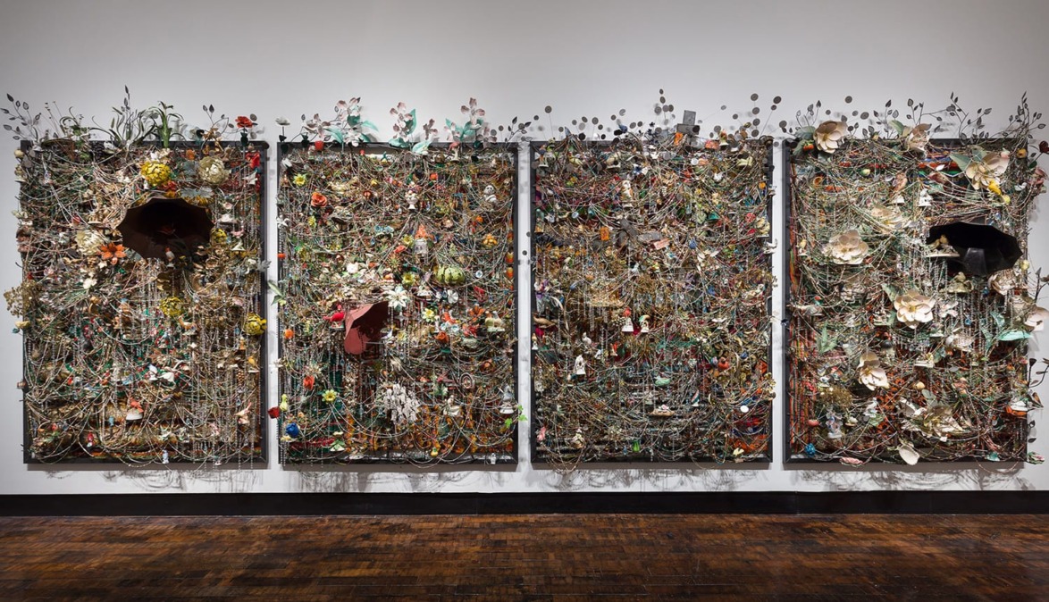 Colorful mixed media art installation with intricate details and various objects on four panels displayed on a gallery wall.