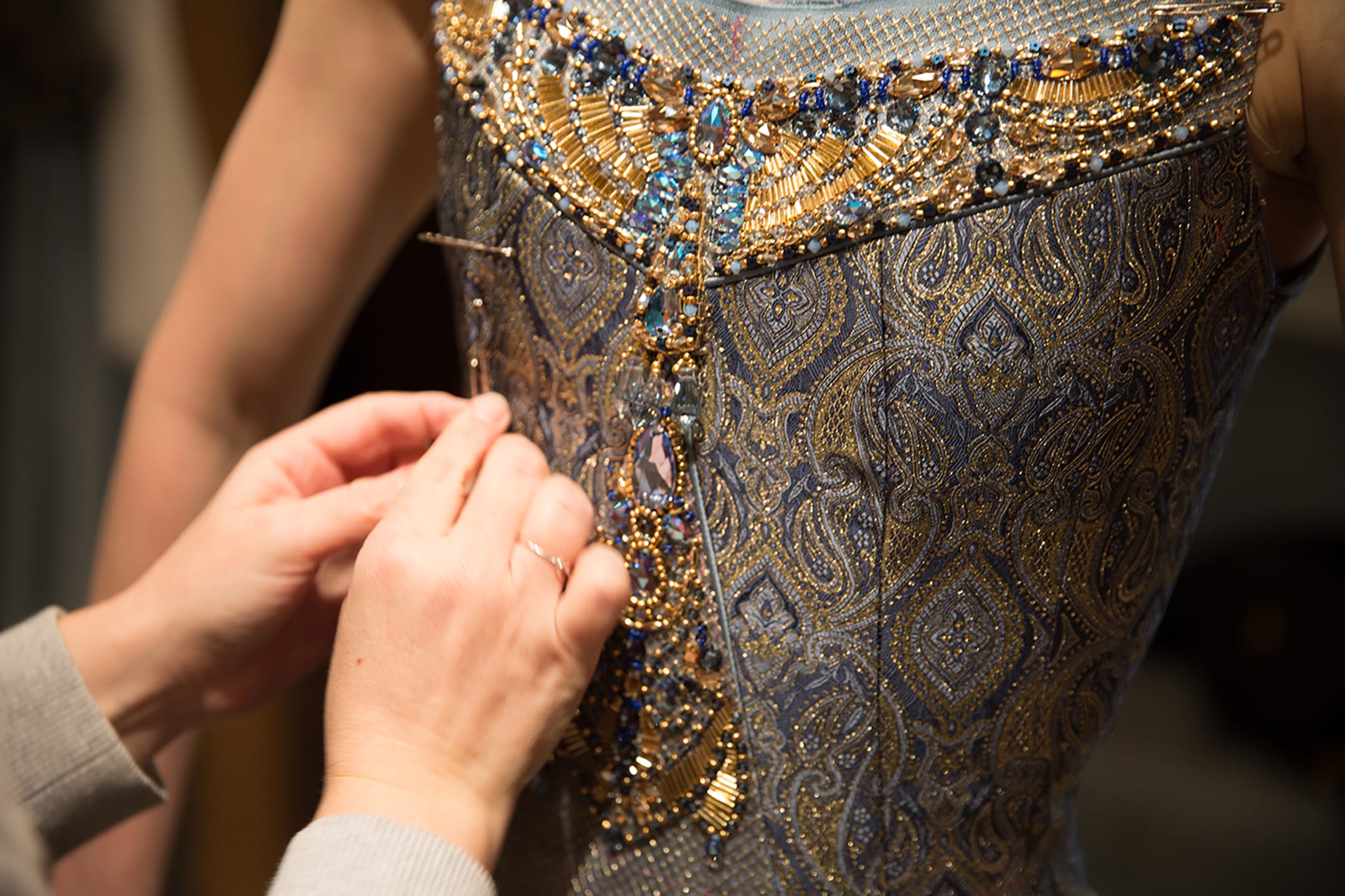 Close-up of hands adjusting intricate beaded details on a blue and gold patterned dress.