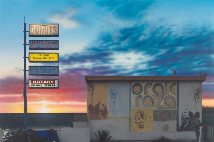 Sunset sky behind vintage signs for donuts, fashion, vacuums, and a mural on a building façade.