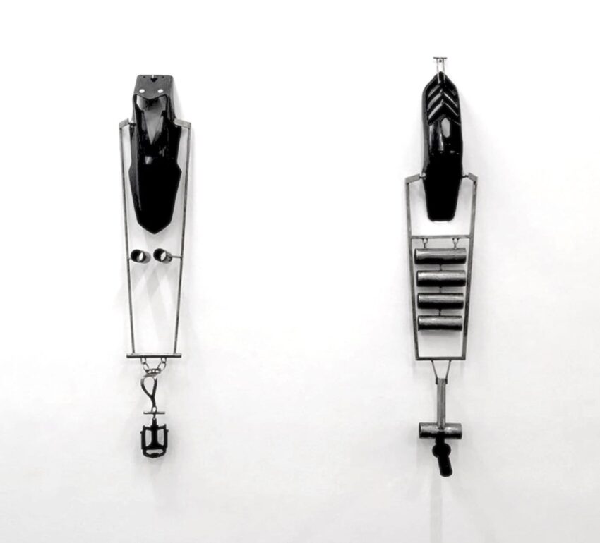 Two abstract sculptures mounted on a white wall, featuring metal components and black elements.