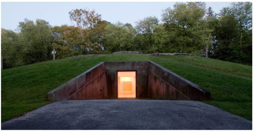 Illuminated entrance to an underground bunker, surrounded by grassy landscape and trees in the background.