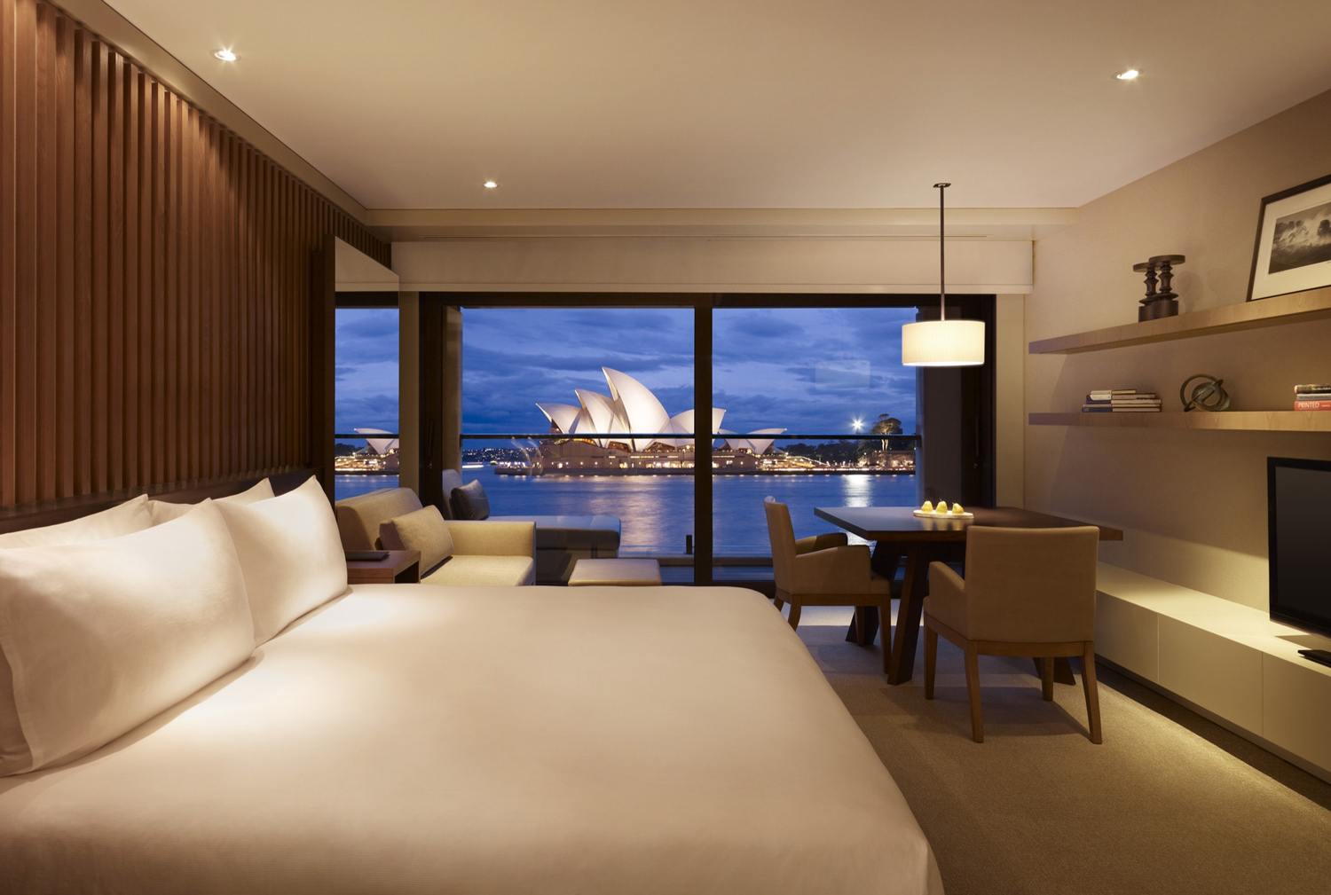 Luxurious hotel room with a stunning view of the Sydney Opera House across the water at twilight.
