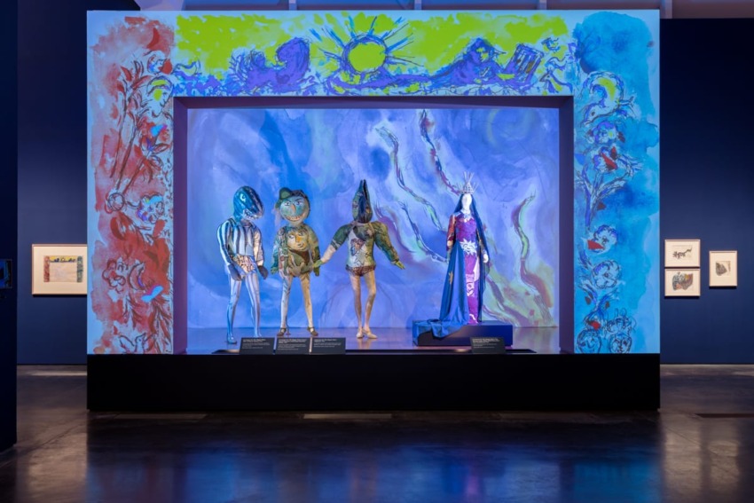 Colorful art installation featuring four abstract humanoid figures with a vibrant backdrop in a museum setting.