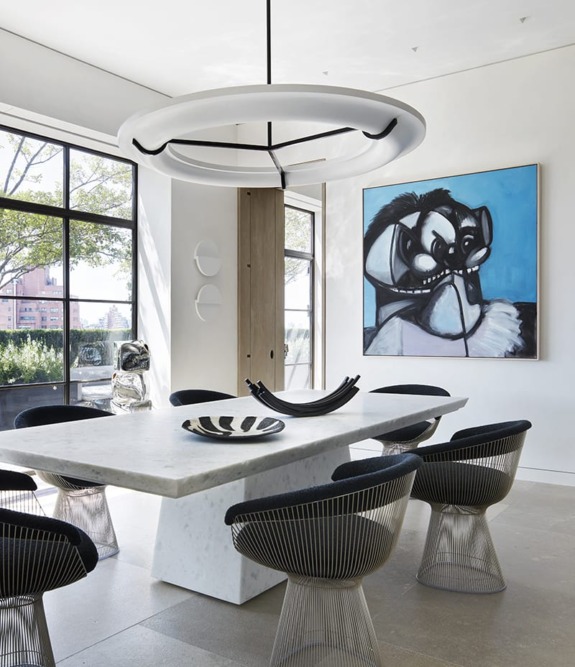Modern dining room with a marble table, stylish chairs, abstract painting, and large windows with a city view.