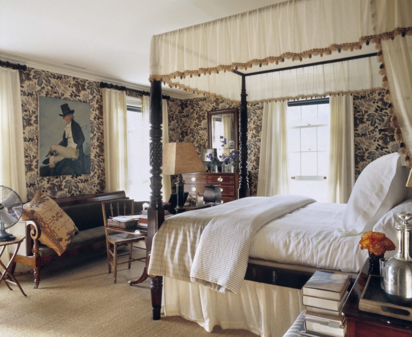 Elegant bedroom with a four-poster bed, floral wallpaper, large windows, and a cozy seating area.