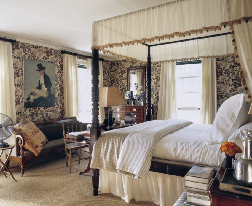 Elegant bedroom with a four-poster bed, floral wallpaper, large windows, and a cozy seating area.