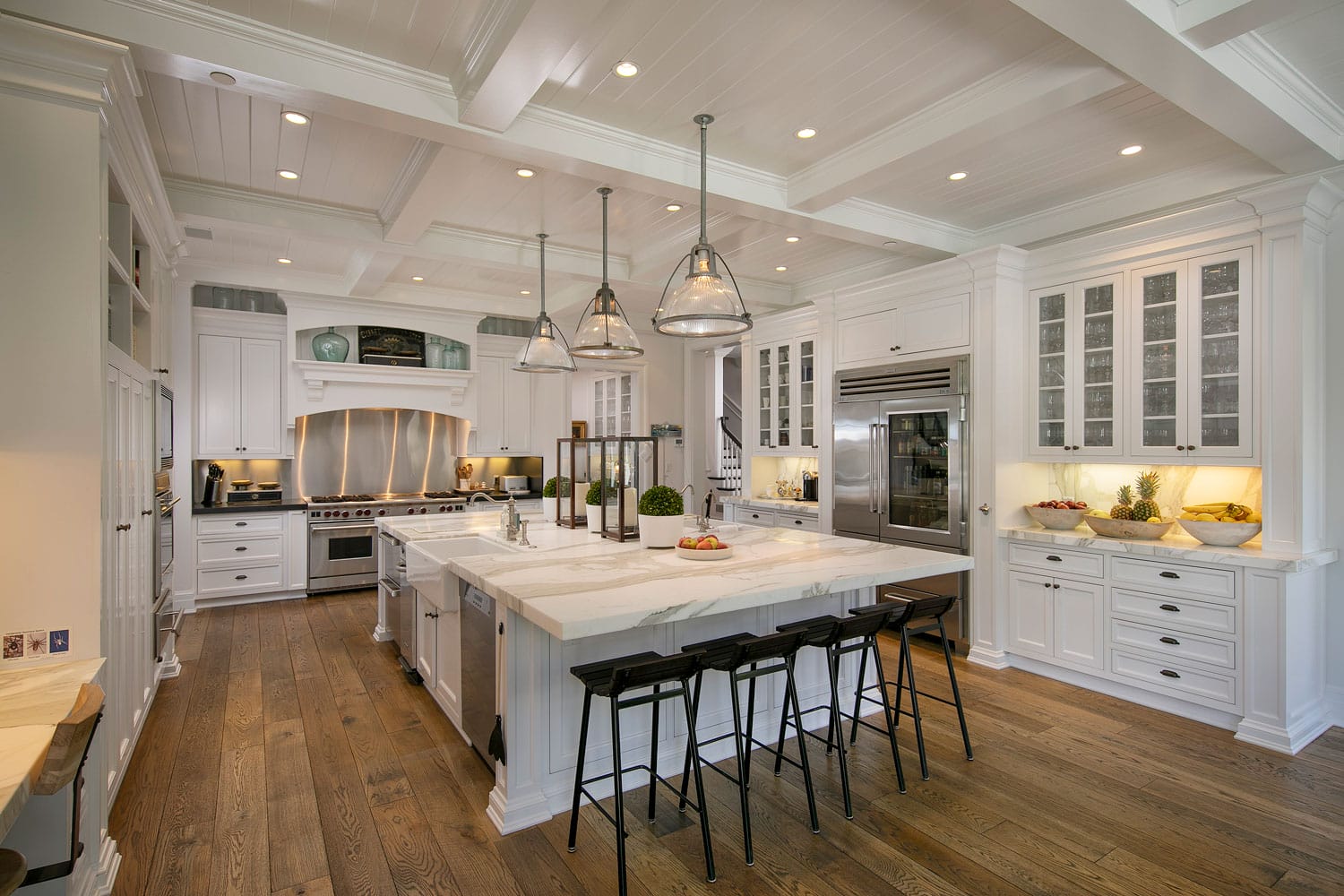 Spacious modern kitchen with white cabinets, large island, pendant lights, and wooden flooring.