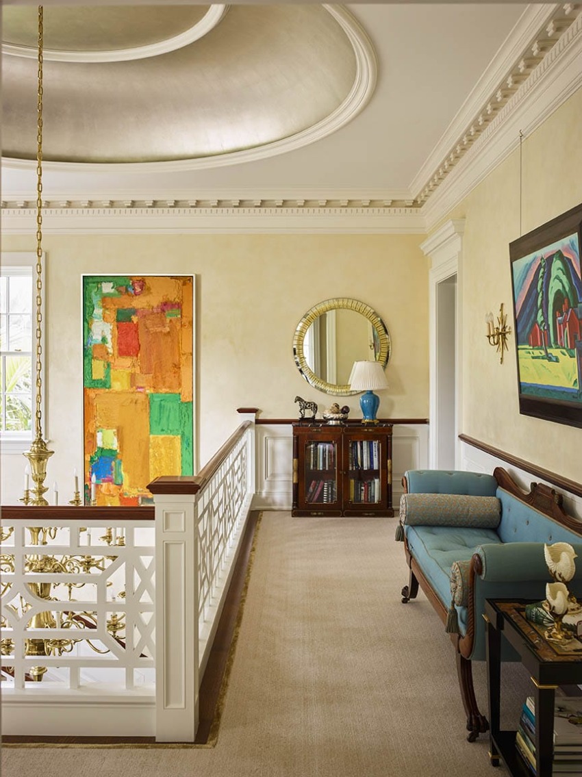Elegant hallway with colorful abstract paintings, a blue sofa, ornate ceiling, and decorative mirror above a cabinet.