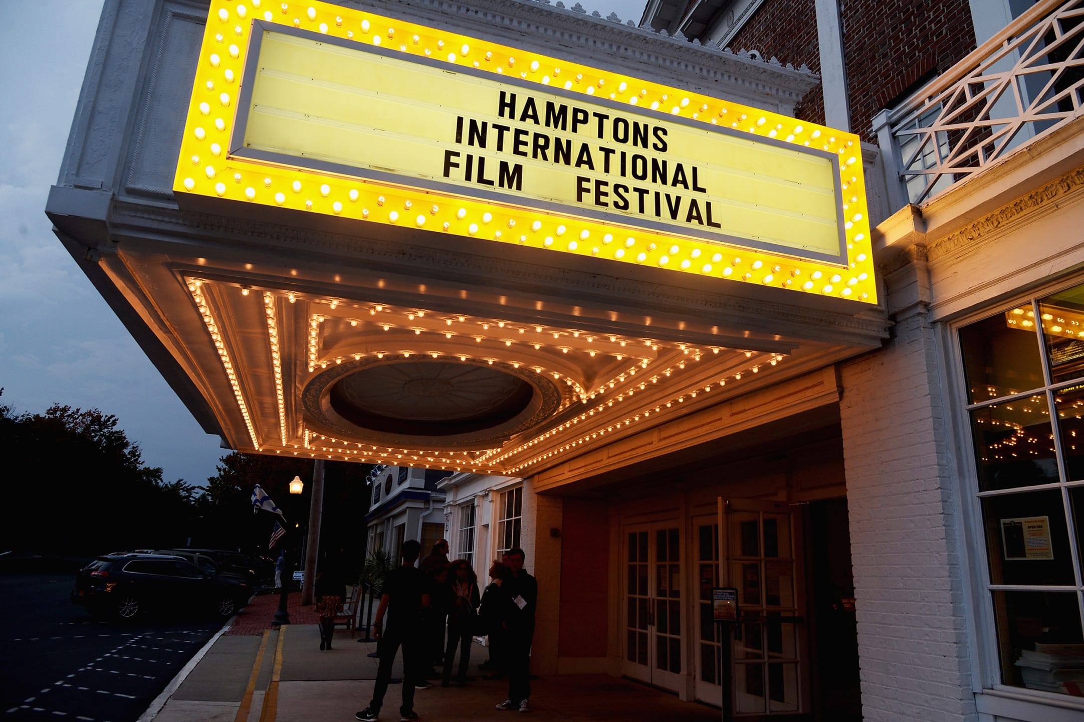 Marquee with "Hamptons International Film Festival" sign illuminated at the entrance of a theater building at dusk.
