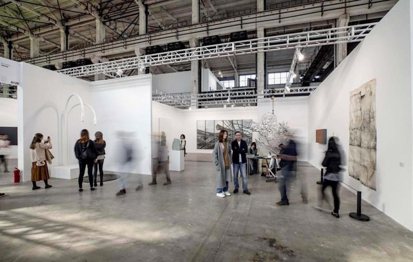 People walking through a contemporary art exhibition in a large industrial-style gallery space.